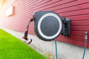 Wall Mounted Retractable Hose Reel. Modern garden lawn watering tip hose with sprinkler hanged at...