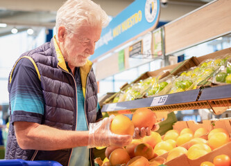 Senior man selecting grapefruits or oranges in supermarket shopping for groceries selecting fruit...