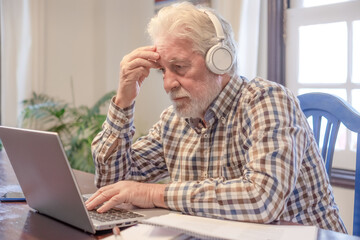 Fototapeta premium Video call concept. Concentrated man sitting at table with laptop and books working or studying in video connection. Attractive senior man enjoying teaching activity and learning using new technology