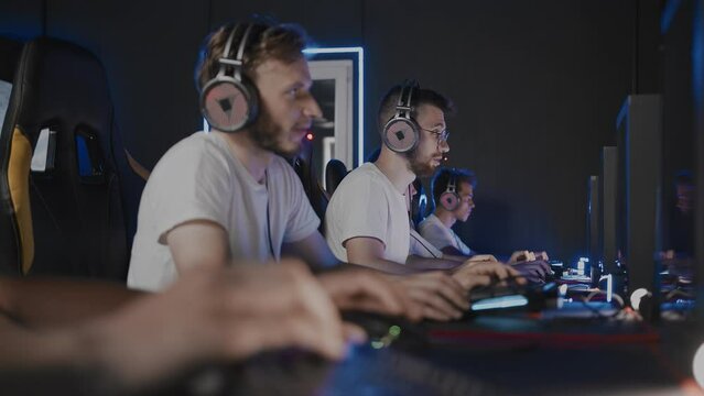 Bristly gamers playing video game on PC at computer club, cyber sport tournament. E-sport team at championship. Five players in headset. Multiplayer online first-person shooter, real-time strategy RTS