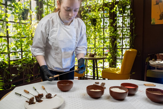 Confectioner makes sweets from natural products decorating with coconut flakes. Production of craft sweets in modern workshop