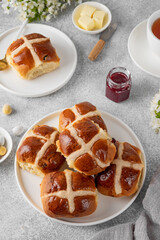 Traditional Easter hot cross buns on a white plate with butter, berry jam and cup of tea. Delicious Easter breakfast.