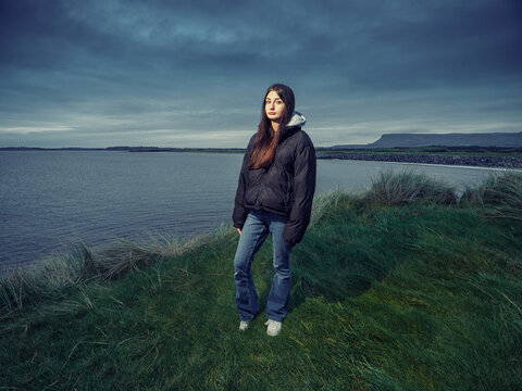 Teenager girl tourist explore stunning sights of Ireland. Rosses point, county Sligo, Ireland. Beach and Benbulben flat top mountain in the background. Dark and moody sky. Travel and sightseeing
