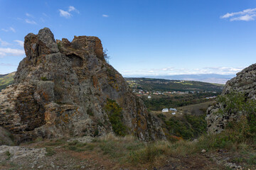 Landscape view through the rocks from the ruins of Kojori fortress. Bright blue sky and clouds. Mountains, rocks, villages in the valley and a line of clouds on the horizon. Colored bushes