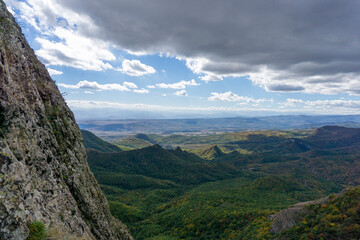 Landscape view from the ruins of Kojori fortress. Bright blue sky and clouds. Mountains, rocks, villages in the valley and a line of clouds on the horizon. Colored bushes and green grass.