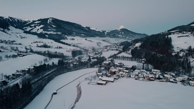 Drone slowly circling around a snow covered village in the mountain ranges of Leogang, Austria, with cars driving on the road