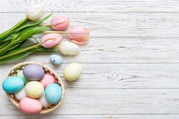 Happy Easter composition. Easter eggs in basket on colored table with yellow Tulips. Natural dyed colorful eggs background top view with copy space