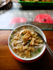 Typical Semarang soto ayam or chicken soto, with clear soup, suitable for breakfast, lunch or dinner. popular food in Indonesia. With fried garlic topping served in small bowl on wooden table.