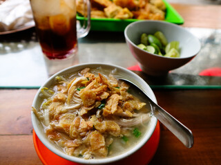 Typical Semarang soto ayam or chicken soto, with clear soup, suitable for breakfast, lunch or dinner. popular food in Indonesia. With fried garlic topping served in small bowl on wooden table.