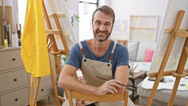 Middle-aged man with beard painting on canvas in sunlit art studio