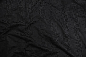 Texture of black taffeta (silk) fabric with black polka-dot pattern, top view. Background, texture of draped dressy fabric with shining black polka-dot pattern.