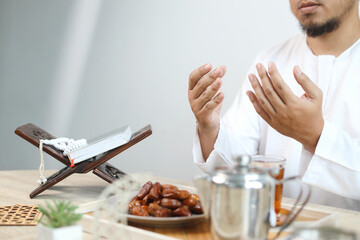 Iftar dish with muslim man hand praying to Allah. Dates fruit with glass of hot tea on the table. 