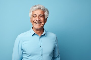 Portrait of smiling senior man with grey hair and blue shirt on blue background - Powered by Adobe