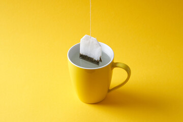 Tea bag in a yellow mug on a yellow background.