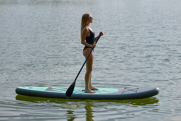 Silhouette of a sporty woman who swims on a sap board on a river on a sunny day. A healthy person,...
