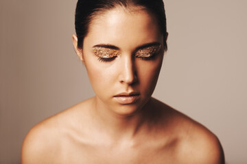 Woman, makeup and gold glitter on eyes for beauty, cosmetology and glamour with cosmetics on beige...