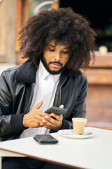 a man with afro hair using a mobile phone while having a latte for breakfast