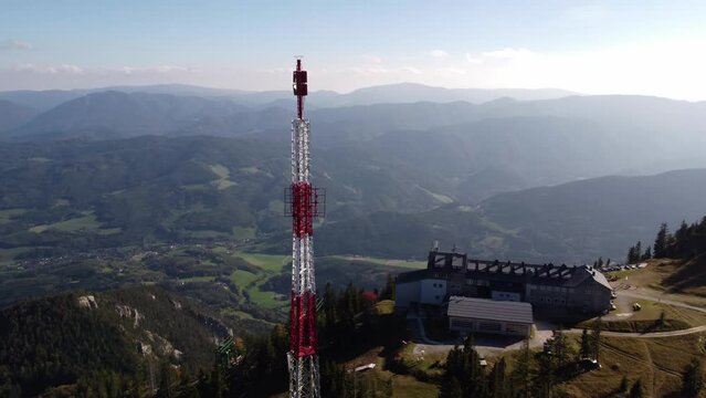 Drone ascending and circling around a Radio tower with a mountain lodge in the background, on the top of Rax mountain