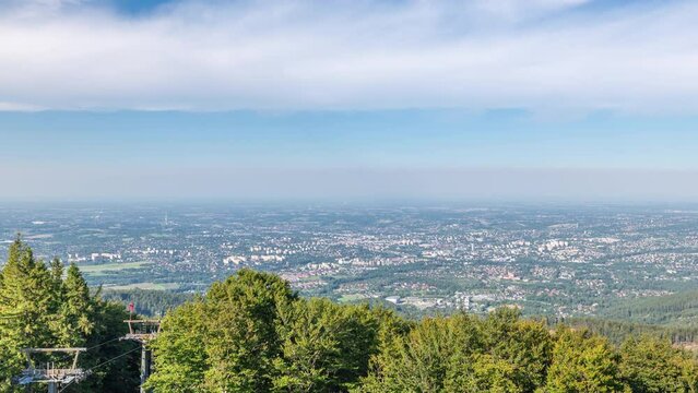 Beautiful aerial panorama seen from Szyndzielnia Mountain timelapse. Upper station of cable car and forest in the foreground, Bielsko - Biala and Beskidy Mountains in the background. Clouds on the sky