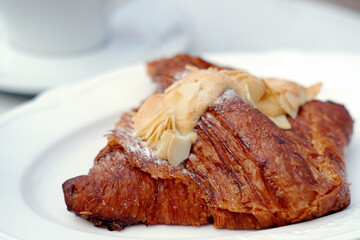 incredibly delicious almond croissant made from sheet puff pastry with a delicate filling, decorated with almond petals on a white plate close-up