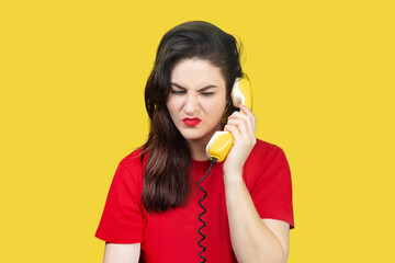 Woman with red lipstick speaks on an old yellow telephone with a cord. Woman is unhappy, does not want to listen to her interlocutor, gets angry. Unwanted call on a yellow background