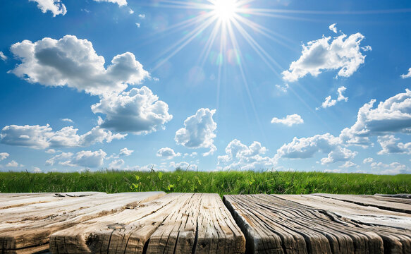 Wooden table over green grass field and bright blue sky with clouds