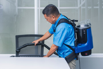 A professional janitor in a blue uniform using a commercial backpack vacuum to clean a modern...