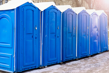 Row of blue clean outdoor portable toilets in winter with bright blue doors and white roof at urban...