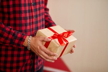 Close-up of hands holding a gift box with a red ribbon against a red background.