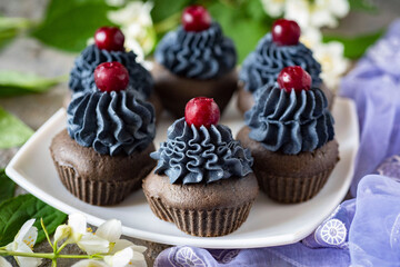 Sweet dessert for breakfast for the whole family: chocolate cupcakes with black cream and cherries. Close-up