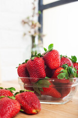 Bowl of strawberries by the window through which the light enters and illuminates the scene.