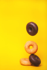 Vertical photograph of sugar and chocolate doughnuts falling one on top of the other in a pile on a vibrant yellow background.