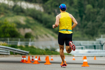 Fototapeta premium rear view athlete running on asphalt with orange safety cones, mountain marathon race