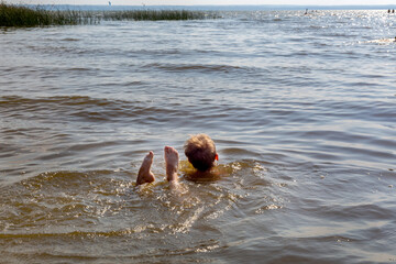 Boy learns to swim in river in summer. His legs stick out of water in funny way