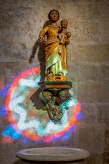 Virgin and child statue illuminated by the colorful light of a stained glass window in the church of Saint-Paul de Vence, France - 758798271