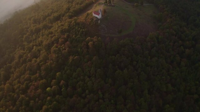 Aerial view of St. Anne's Church (Cerkev sv. Ane) on top of a mountain with low fog, Jezero, Slovenia
