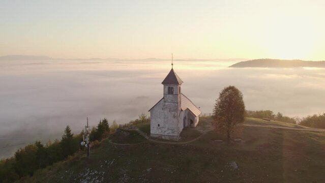 Aerial view of St. Anne's Church (Cerkev sv. Ane) on top of a mountain with low fog, Jezero, Slovenia