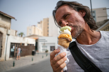 An adult man eats ice cream against the backdrop of the city. It's hot, summer.