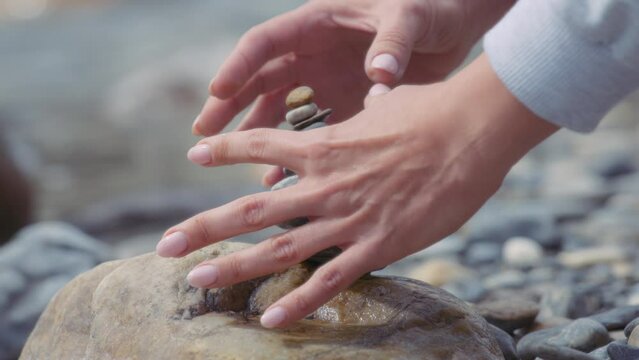 Woman's hands creating a stack of balanced stones near the river. Slow motion. 