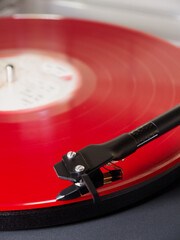 Closeup of a red vinyl LP record on a turntable, with the tonearm needle or stylus positioned at...