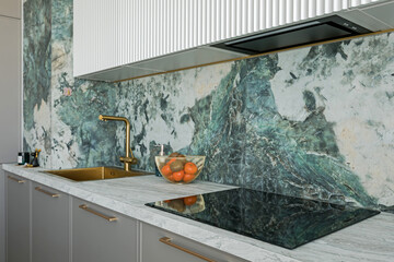 Grey kitchen table top with electric stove with a hood and sink, against a green marble tiled wall
