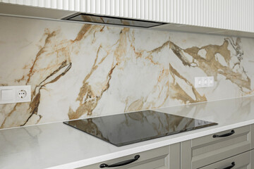 Stone kitchen table top with electric stove and hood, against a marble tiled wall - 758809264