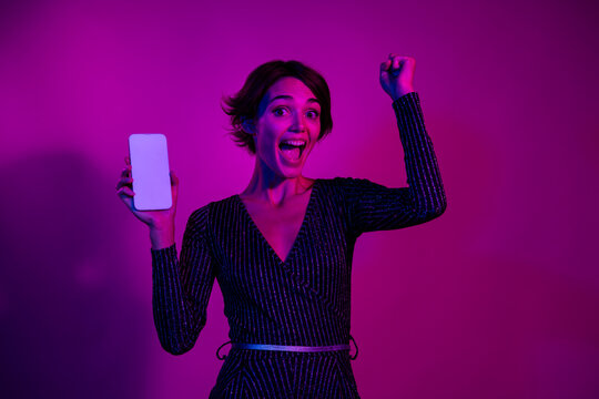 Photo portrait of pretty young girl raise fist hold white screen wear trendy overall outfit isolated on neon light pink color background