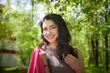 Fototapeta premium Joyous brunette woman near Blossoms of apple tree in a Spring Garden outdoors. Concept of face and body care. The scent of perfume and tenderness