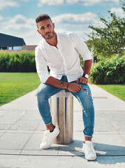 A man is seen sitting on a tall metal pole, balancing carefully as he looks down. The urban setting...