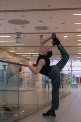 Fototapeta na wymiar A young androgynous teenage male dancer doing acrobatic dancing poses indoors in a shopping center