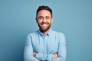 Portrait of a handsome smiling man with crossed arms against blue background - obrazy, fototapety, plakaty