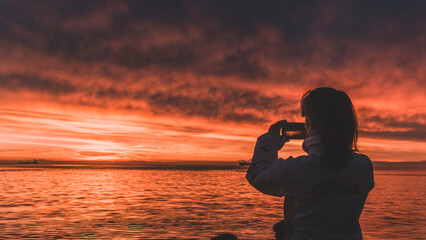 A woman taking a picture of a red sunset over the sea in Trieste, Italy
