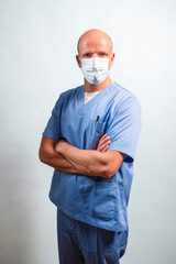 Portrait of a physiotherapist in light blue gown and face mask looking at camera in studio.