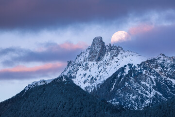 Beautiful view of the full moon partially covered over the Pierre Avoi mountain at sunset - obrazy, fototapety, plakaty
